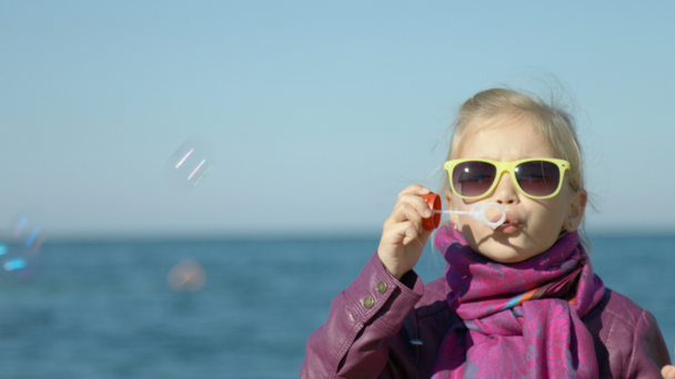 海のビーチで泡を吹いているサングラスの女の子の肖像画。カメラ目線の子 - 映像、動画