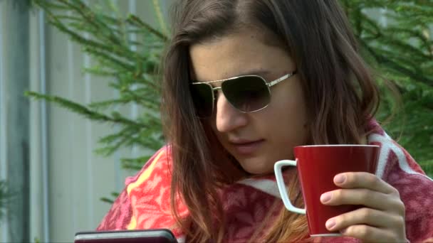 Close up shot girl face in sunglasses reading tablet pc with cup of coffee - Imágenes, Vídeo