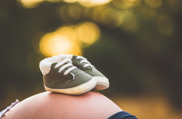 Donna incinta con scarpa per bambini sullo stomaco
 - Foto, immagini