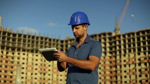 Architect met een tablet op een achtergrond van een onder bouw huis. Bouw, foreman werknemer met tablet pc op een bouwplaats. Ingenieur kijken naar tablet. Modern gebouw.   - Video
