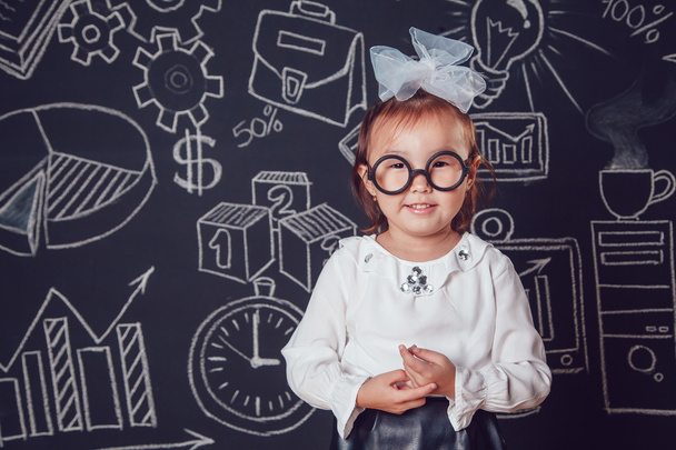 The little smart girl in glasses on a background of wall with business or school picture - 写真・画像