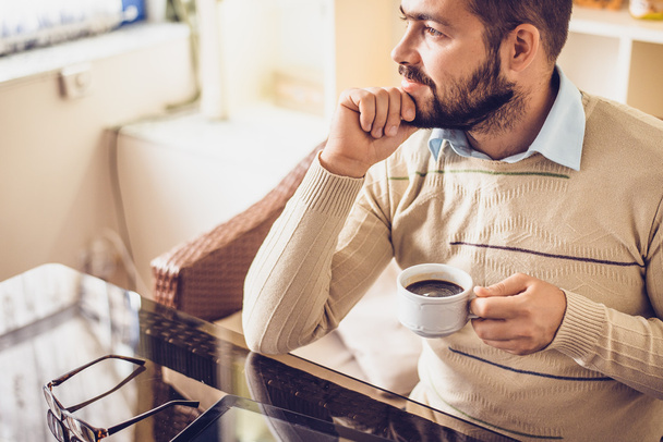бородатый мужчина сидит с чашкой утреннего кофе и смотрит в окно
 - Фото, изображение