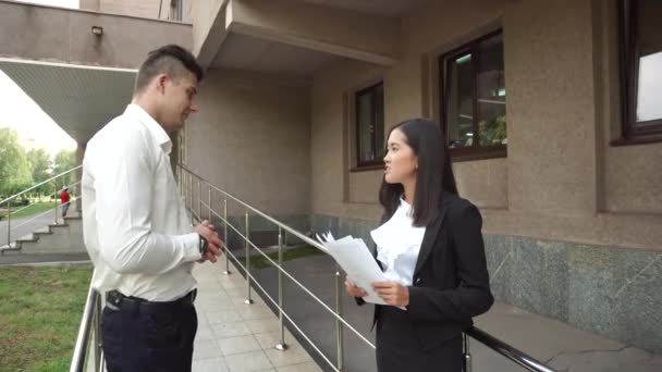 Jonge mooie Aziatische Business vrouw vrouw en Kaukasische mannelijke blik op documenten spreken op kantoorgebouw trappen - Video
