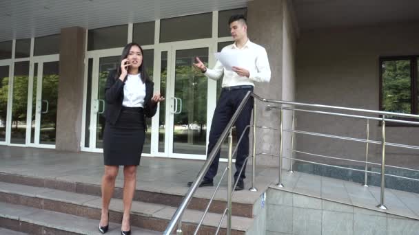 Young Beautiful Asian Business Woman Female and Caucasian Male Look at Documents, Talk on Phone Office Building Stairs - Πλάνα, βίντεο