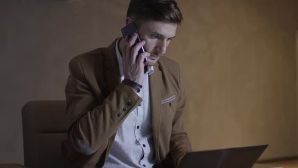 Businessman is talking on the phone while using a laptop computer. - Záběry, video