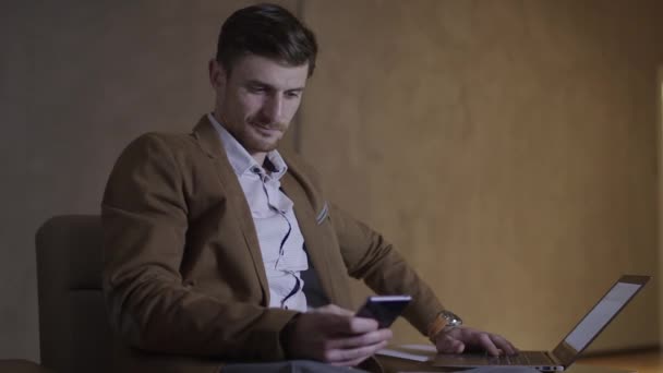 Businessman is using both his mobile nad a laptop computer. - Materiał filmowy, wideo