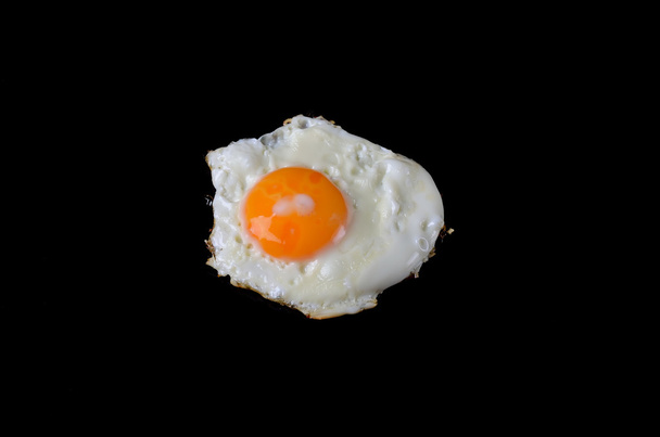 Fried egg on a black background, delicious breakfast. - Foto, afbeelding