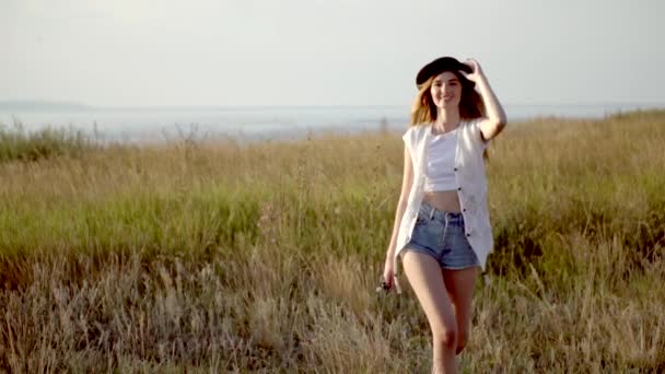 Joven hermosa chica modelo en sombrero runnig y bailando en el prado cerca del río
 - Metraje, vídeo