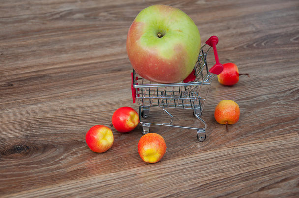 Gran manzana en el carrito de la compra y pequeñas manzanas a su alrededor
 - Foto, imagen