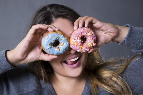 Happy beautiful young caucasian plus size model posing with donuts on a gray studio background - 写真・画像