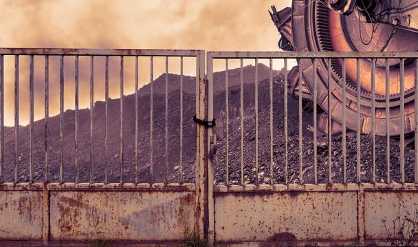  Escavatore gigante della ruota della benna per scavare il carbone marrone dietro un cancello di ferro
 - Foto, immagini