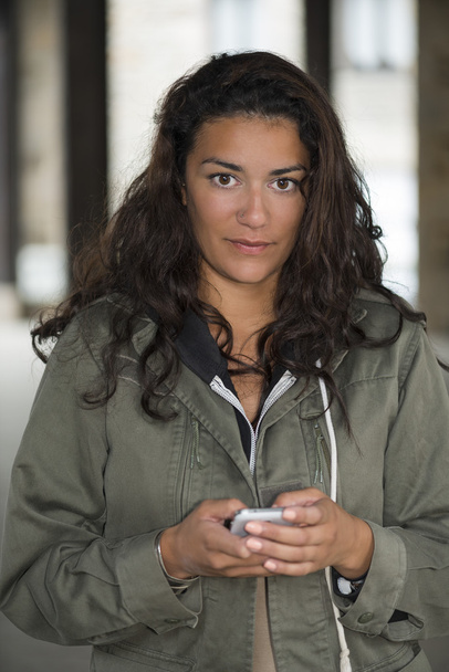 Jonge vrouw in hal holding haar smartphone en denken - Foto, afbeelding