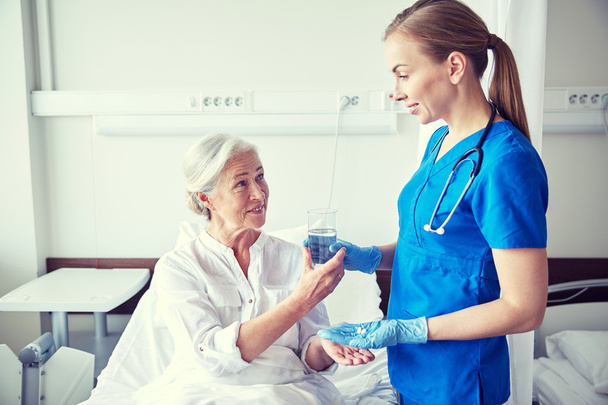verpleegkundige geeft geneeskunde aan senior vrouw in het ziekenhuis - Foto, afbeelding