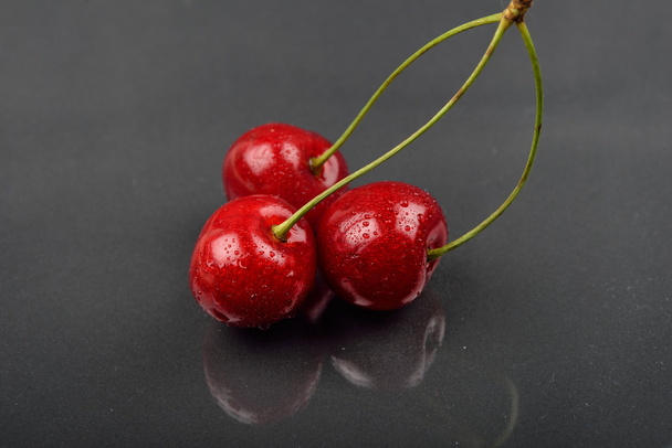 Three red cherries with water drops against reflective black bac - Фото, изображение