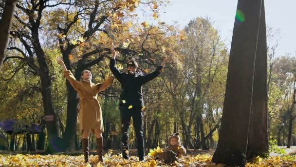 Familia feliz jugando con hojas de otoño en el parque. Mamá y papá vomitan leas en el aire. Pequeño niño mirarlos y divertirse
. - Metraje, vídeo