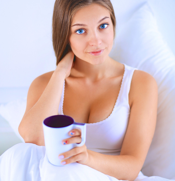 A pretty young woman in bed enjoying a cup of tea - Фото, изображение