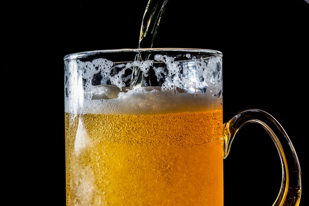 Stream of beer being pouring into a glass with beer and foam isolated on black background - Fotografie, Obrázek