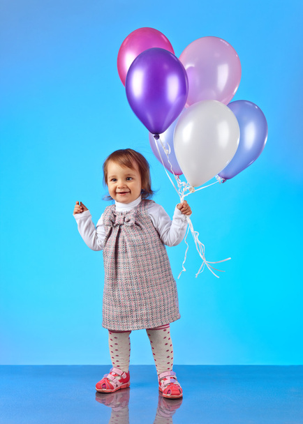  klein meisje met ballonnen op een blauwe achtergrond - Foto, afbeelding
