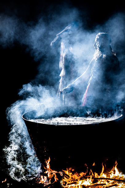 Beautiful witch brew a potion in the big cauldron. ? lot of amulets on enchantress hands. Boiling elixir in the pot. Beldam lead his hands. Sibyl looking to the side. - Photo, Image