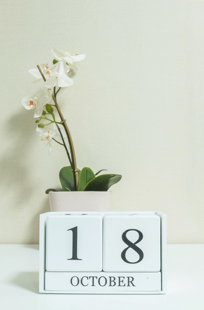 Gros plan calendrier en bois blanc avec mot noir 18 octobre avec fleur d'orchidée blanche sur bureau en bois blanc et papier peint de couleur crème dans la chambre fond texturé, voir une autre date dans mon portefeuille
 - Photo, image