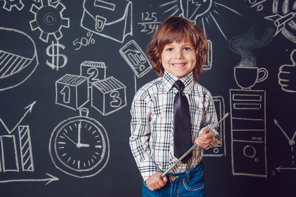 Little boy as a businessman or teacher standing and holding pointer on dark background with business school picture - Zdjęcie, obraz