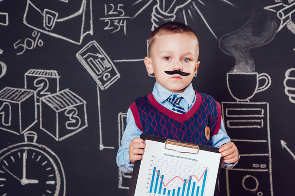 Kleine jongen als zakenman met snor toont grafiek van de Companys zakelijke activiteiten op donkere achtergrond patroon - Foto, afbeelding