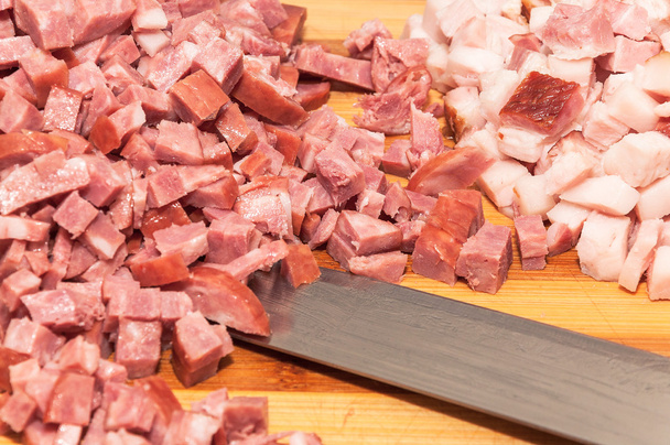 Tocino y salchicha italiana en trozos pequeños en la tabla de cortar y un cuchillo de acero
 - Foto, Imagen