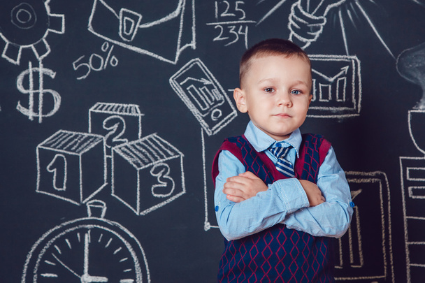 Kleine jongen als zakenman of leraar staan met haar handen gevouwen op een donkere achtergrond patroon - Foto, afbeelding
