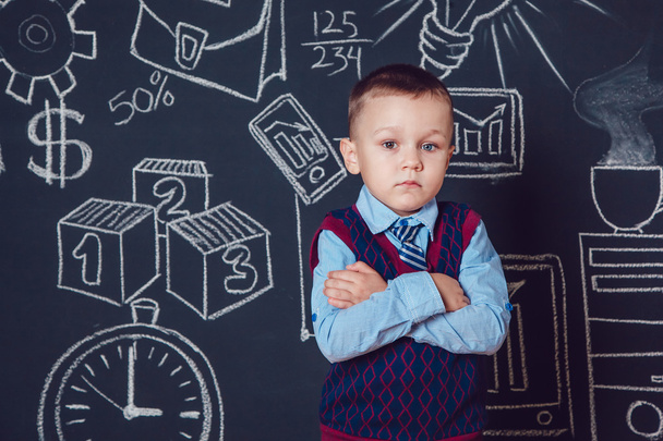 Kleine jongen als zakenman of leraar staan met haar handen gevouwen op een donkere achtergrond patroon - Foto, afbeelding