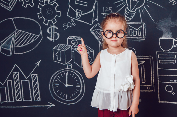 The little smart girl lifting finger up on a background of wall with business or school picture - Foto, Imagen