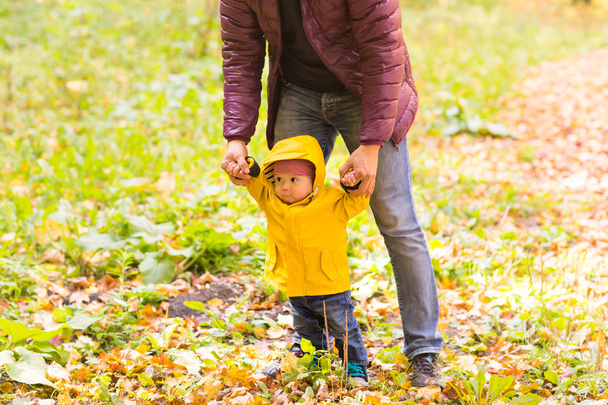 Otce a syna chůzi. Dítě při první kroky s pomocí otce na podzim zahrady ve městě - Fotografie, Obrázek