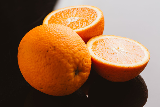 φέτες πορτοκαλιού στα ημίχρονα και ολόκληρη σε ένα closeup σκούρο φόντο - Φωτογραφία, εικόνα