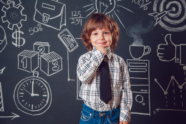 Chlapeček jako obchodník nebo učitel nosí košili a kravatu a drží bradu na tmavém pozadí s obrázkem obchodní školy. - Fotografie, Obrázek