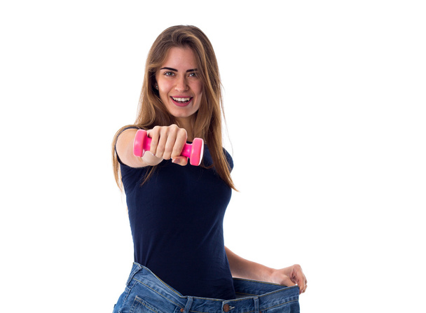 Woman wearing jeans of much bigger size and holding a dumbbell - Photo, Image