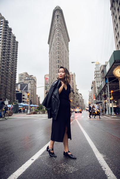 Fashionable asian woman crossing New York City street at Manhattan wear leather jacket and black dress. Woman looking to the side. - Fotoğraf, Görsel