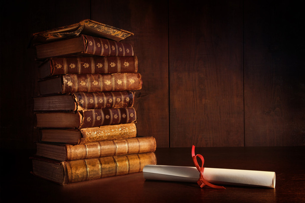 Купка старих книг і диплом на столі
 - Фото, зображення