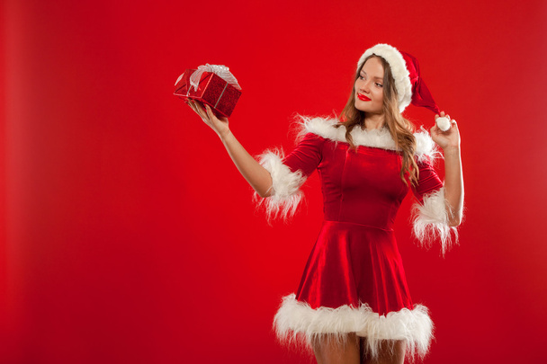 Noël, Noël, hiver, concept de bonheur - femme souriante dans un chapeau d'aide Père Noël avec boîte cadeau, sur fond rouge
 - Photo, image