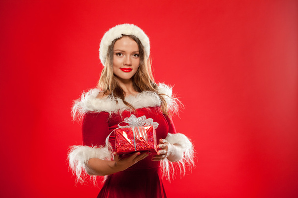 christmas, x-mas, winter, happiness concept - smiling woman in santa helper hat with gift box, over red background - Foto, imagen
