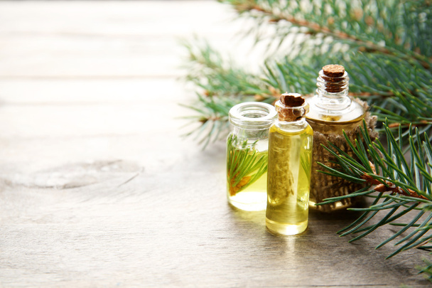 Bottles of coniferous essential oil and branches on wooden background, close up view - Valokuva, kuva