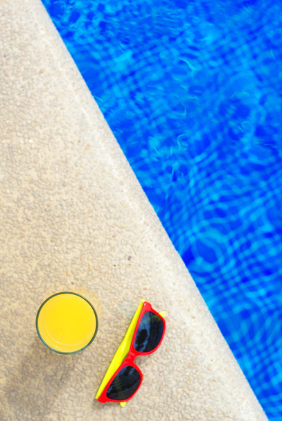 Jus d'orange en zonnebril in de buurt van het zwembad. Ruimte voor tekst. - Foto, afbeelding