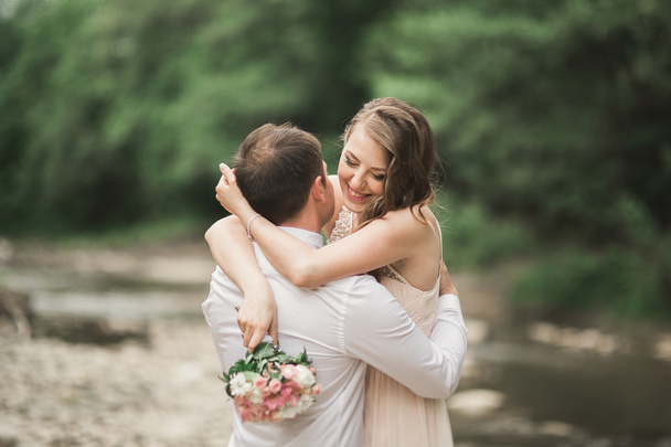 Elegant gentle stylish groom and bride near river with stones. Wedding couple in love - Fotografie, Obrázek