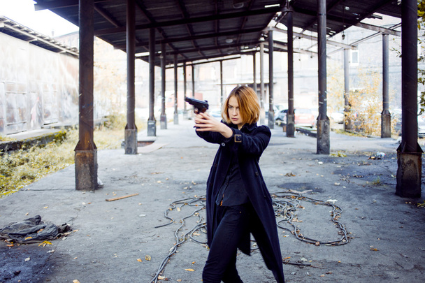 Woman pointing a gun. Mafia girl shooting at someone on the street. - Фото, изображение