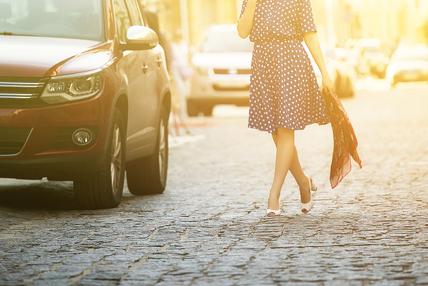 young beautiful woman in a blue sundress walking down the street next to the car, holding a sweater in his hands - Photo, image