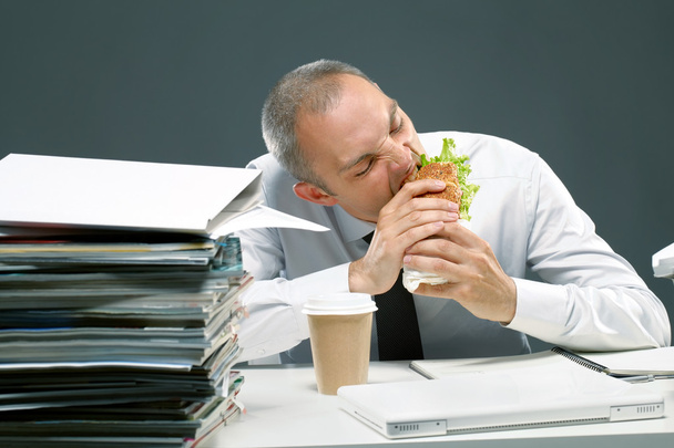 Γραφείο εργαζόμενος τρώει σάντουιτς στο γραφείο του - Φωτογραφία, εικόνα