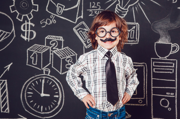Little boy as businessman or teacher with mustache and glasses standing on a dark background pattern. Wearing shirt, tie - Фото, изображение