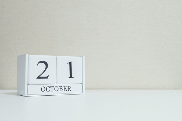 Closeup white wooden calendar with black 21 october word on blurred white wood desk and cream color wallpaper in room textured background with copy space , selective focus at the calendar - Photo, Image