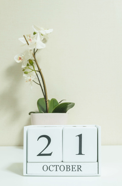 Gros plan calendrier en bois blanc avec noir 21 mot d'octobre avec fleur d'orchidée blanche sur bureau en bois blanc et papier peint de couleur crème dans la chambre fond texturé, mise au point sélective au calendrier
 - Photo, image