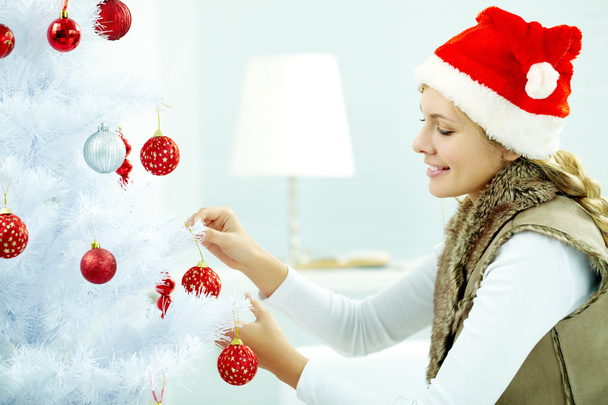 Woman hanging Christmas balls on a tree - 写真・画像