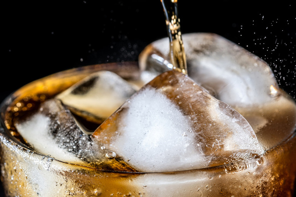Stream of soda being pouring into a glass with soda and ice cube on black background, closeup texture, splashing, splash, fizz  - Fotografie, Obrázek