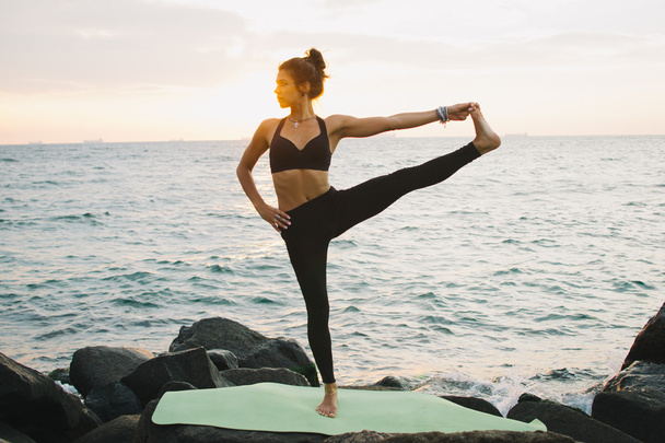 Молодая женщина практикует йогу на скалистом побережье на рассвете или на закате
 - Фото, изображение